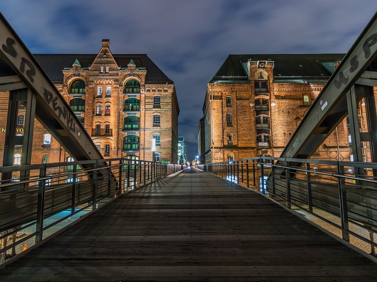 Night view from a steel pedestrian bridge between two illuminated brick warehouse buildings